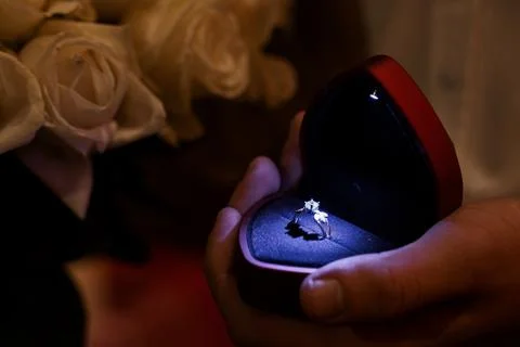 Romantic proposal moment with diamond ring in heart-shaped box and white ro.. Stock Photos