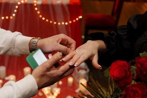Romantic Proposal Moment with Ring Being Placed on Woman's Finger Amidst Re.. Stock Photos