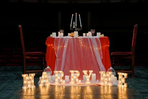 Romantic proposal setup with illuminated "MARRY ME" letters, candlelit tabl.. Stock Photos