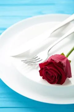 Romantic restaurant table setting with red rose on plates, on blue wooden bac Stock Photos