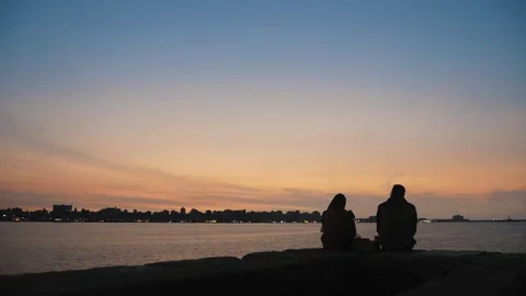 Romantic Scene with Two People Sitting by the Water on the Background of Sunset Stock Footage 243941801