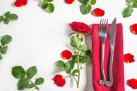 Romantic table setting with original cutlery on red napkin and red rose flowe Stock Photos