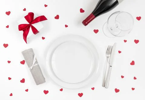 Romantic table setting with red confetti hearts, dinnerware and wine Stock Photos