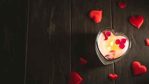 Romantic valentine's day setting featuring a glowing heart-shaped candle surr Stock Photos