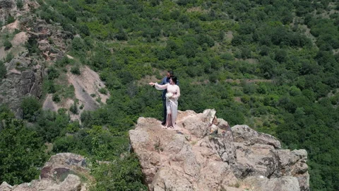 Romantic wedding couple stands on mountain peak rugged cliff holding hands an Stock Footage 335602992