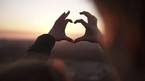 Romantic young couple join hands in a heart shape against the sun standing on Stock Footage 104403637