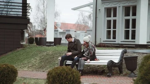 Romantic Young couple sitting on a white bench, in a coat and hat, cold weather Stock Footage 73856548