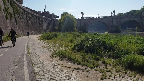 Rome, two bikers ride and a man jogs at morning near Tiber river with a bridge  Stock Footage 108600822