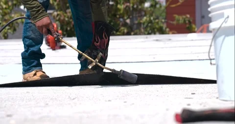 Roofer applying granulated APP Torch Down and Using a Roller Stock Footage 277974177