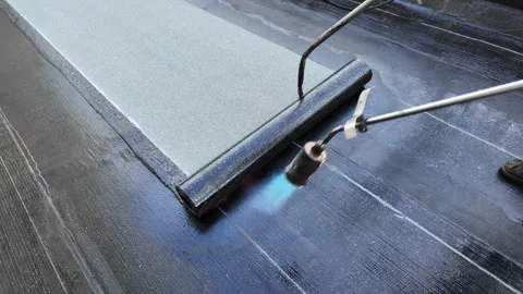 Roofer applying torch to bitumen membrane on torch down roof Stock Footage 317956886