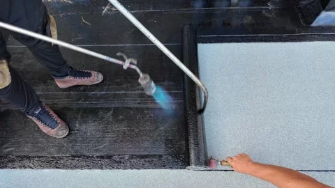 Roofer applying torch to bitumen membrane on torch down roof Stock Footage 317956969