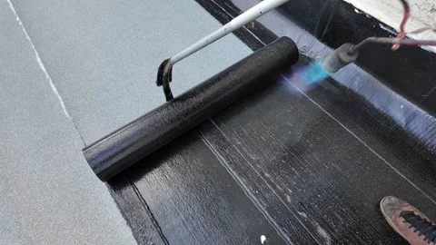 Roofer applying torch to bitumen membrane on torch down roof Stock Footage 317956979