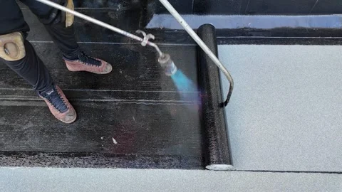 Roofer applying torch to bitumen membrane on torch down roof Stock Footage 317957318