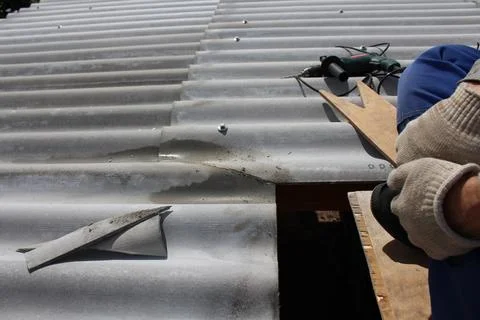 Roofer cutting or fitting a slate piece on a corrugated roof surface during.. Фото