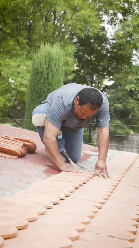 Roofer installing rows of flat clay tiles on rooftop Stock-Footage 345696382
