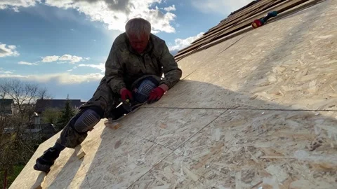 Roofer man sitting on the roof making repairs. Roof renovation and preparation Vídeo Stock 246505358