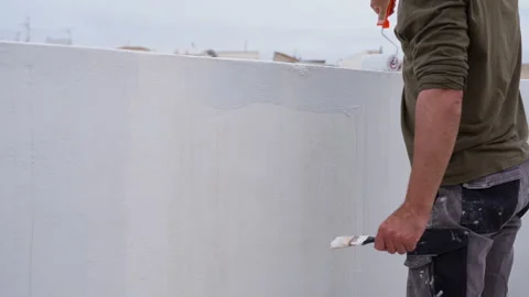 Roofer uses small roller to apply white waterproofing paint on outdoor wall.. Stock Footage 334549820
