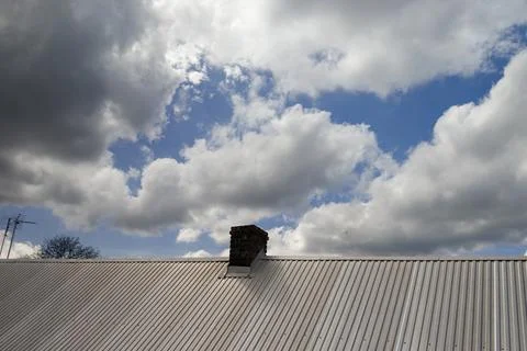 A rooftop with a chimney under a dynamic sky showcasing varied cloud formations, Stockfoto's