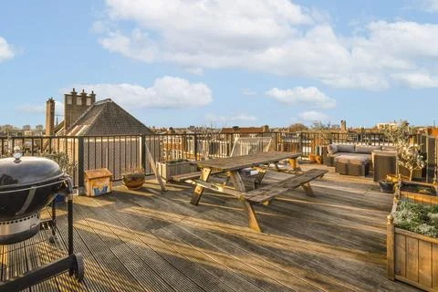 A rooftop deck with a picnic table and a grill Stock Photos