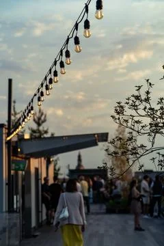 A rooftop gathering at sunset featuring hanging string lights Stock Photos