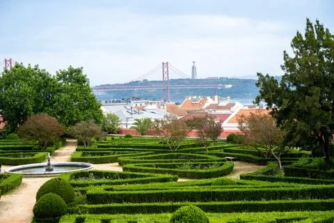 Rooftops and 25 de Abril Bridge above hedges in Belem Lisbon Portugal Stock Photos