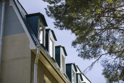 Rooftops of a building are visible with windows under a clear sky. Trees stan Photos