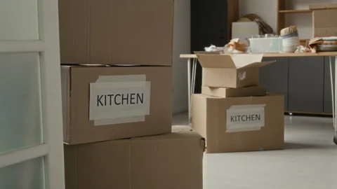 Room with Cardboard Boxes Labeled Kitchen and Dining Table Cluttered with Dishes 動画素材 323296311