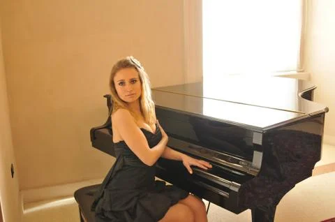 A room with few elements, the only protagonists are a black piano and a young wo 库存照片