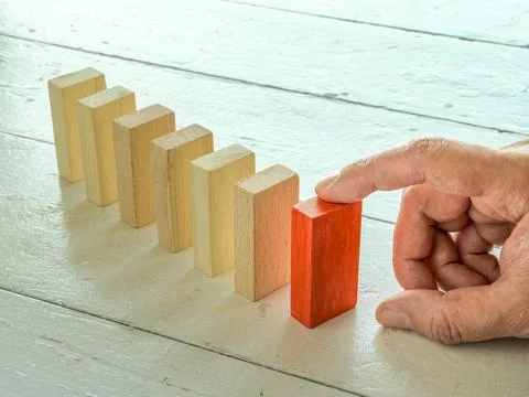 Root cause analysis concept. The finger holds the first tile in the domino line. Stock Photos