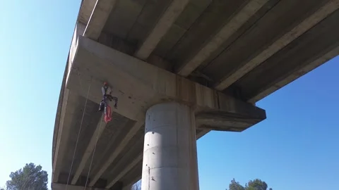Rope access technician inspecting highway overpass support beam Stock Footage 306669566
