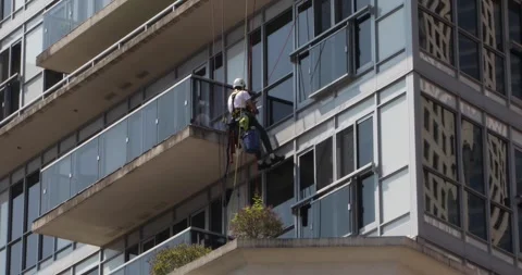 Rope access window cleaner hanging from high-rise condo balcony Video stock 321035655