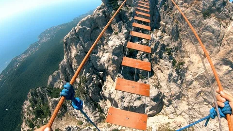 Rope bridge stretched between the rocks.The man carefully crosses the bridge. Stock Footage 95548307