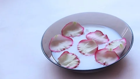 Rose petals float in milk. Video of flower petals in milk. Milk in the plate. Video stock 106567338