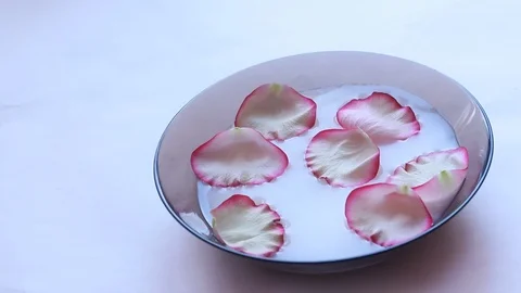 Rose petals float in milk. Video of flower petals in milk. Milk in the plate. Video stock 106567511