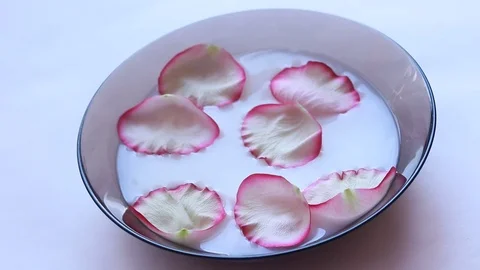 Rose petals float in milk. Video of flower petals in milk. Milk in the plate. Video stock 106567746