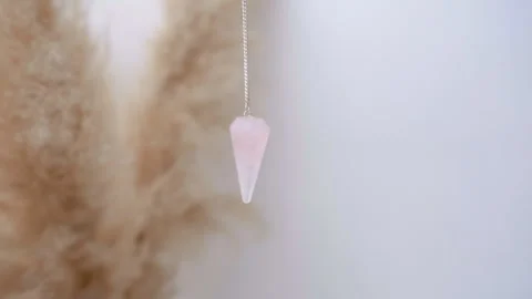 Rose quartz crystal pendulum hanging from a chain swinging in an esoteric Stock Footage 251715450