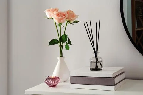 Roses, candle and reed diffuser on white console table in room Stock Photos