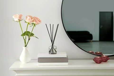 Roses, candles and reed diffuser on white console table in room Stock Photos