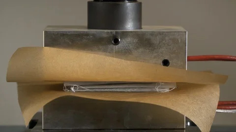 Rosin press lowering down melting marijuana plant onto parchment. Stock Footage 88183007