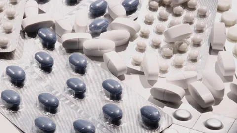 Rotating assortment of tablets and capsules in blister packs and loose on white Stock Footage 310783203