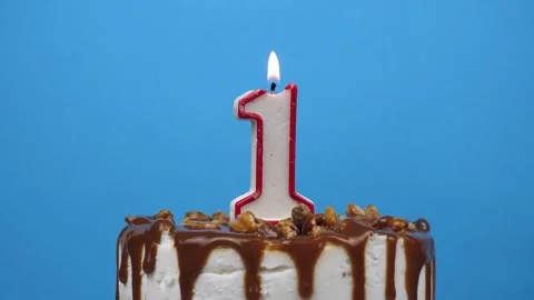 Rotating birthday cake with burning candle number one, 1 on blue background Stock Footage 312237014