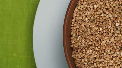 Rotating bowl with buckwheat on white plate on green table cloth. Shooting of Stock Footage 157447963