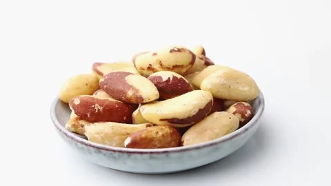 Rotating of brasilian nuts in ceramic plate on white background. Side view. Stock Footage 136050287