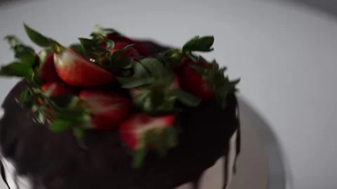 A rotating cake with a glossy chocolate glaze and fresh strawberries on top. The Stock Footage 302794879