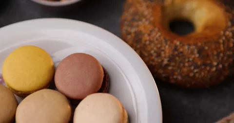 Rotating closeup of macarons on plate with bagel and walnuts, top view motion Stock Footage 320165419