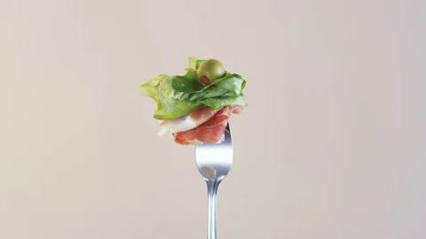 Rotating Fork With Ham and Lettuce on Almond Background Stock Footage 70542345
