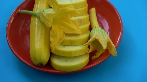 Rotating fresh slice yellow zucchini and flowers in red plate Stock Footage 88610521