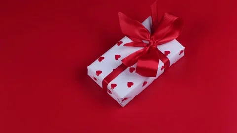 Rotating gift box wrapped in paper hearts and red bow on red background Stock Footage 167522513