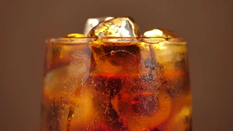 Rotating glass of cola with ice cubes close-up. Cola with ice and bubbles in a Stock Footage 242044029