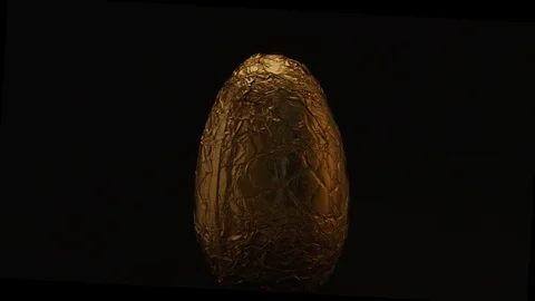 Rotating golden wrapped Easter egg on black background with moody warm top light Stock Footage